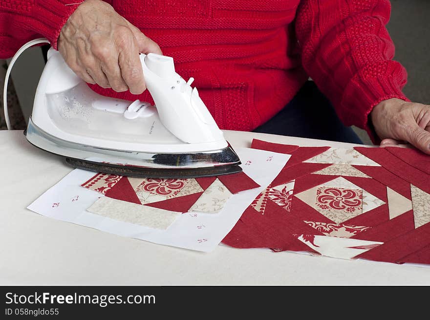 A quilter irons fabric for use in a red and white pieced paper foundation. A quilter irons fabric for use in a red and white pieced paper foundation