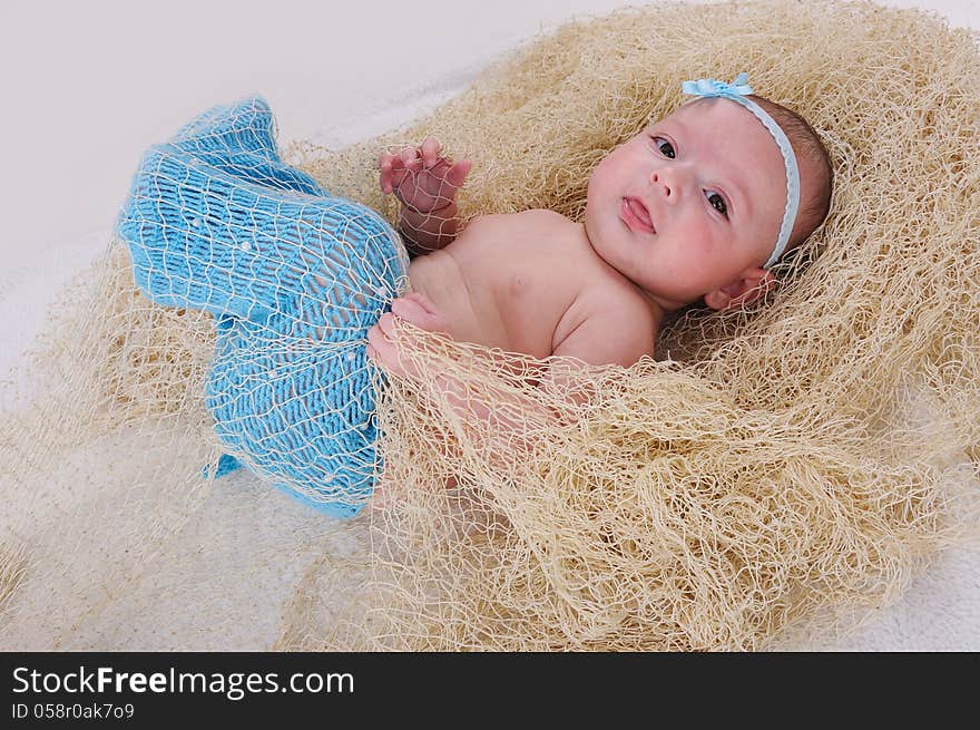 Cute baby girl in net l moves up her knitted blue tail. Cute baby girl in net l moves up her knitted blue tail