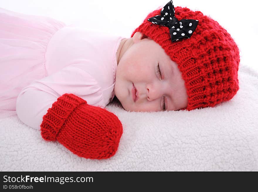 Baby girl dressed in pink dress with red hat and mittens is sleeping. Baby girl dressed in pink dress with red hat and mittens is sleeping