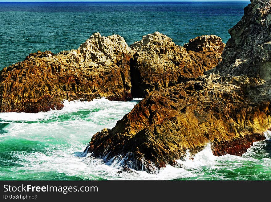 A dramatic landscape scene of a choppy sea with the waves rolling in and crashing against the huge colorful jagged rocky cliff at the point of the coast of the tropical island. Photo taken at Point Lookout, Stradbroke Island, Queensland, Australia. A dramatic landscape scene of a choppy sea with the waves rolling in and crashing against the huge colorful jagged rocky cliff at the point of the coast of the tropical island. Photo taken at Point Lookout, Stradbroke Island, Queensland, Australia.