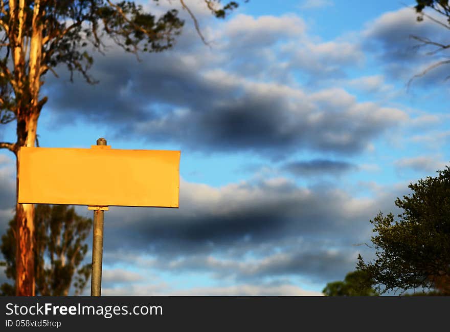 Blank yellow sign with storm clouds & huge Gum tree