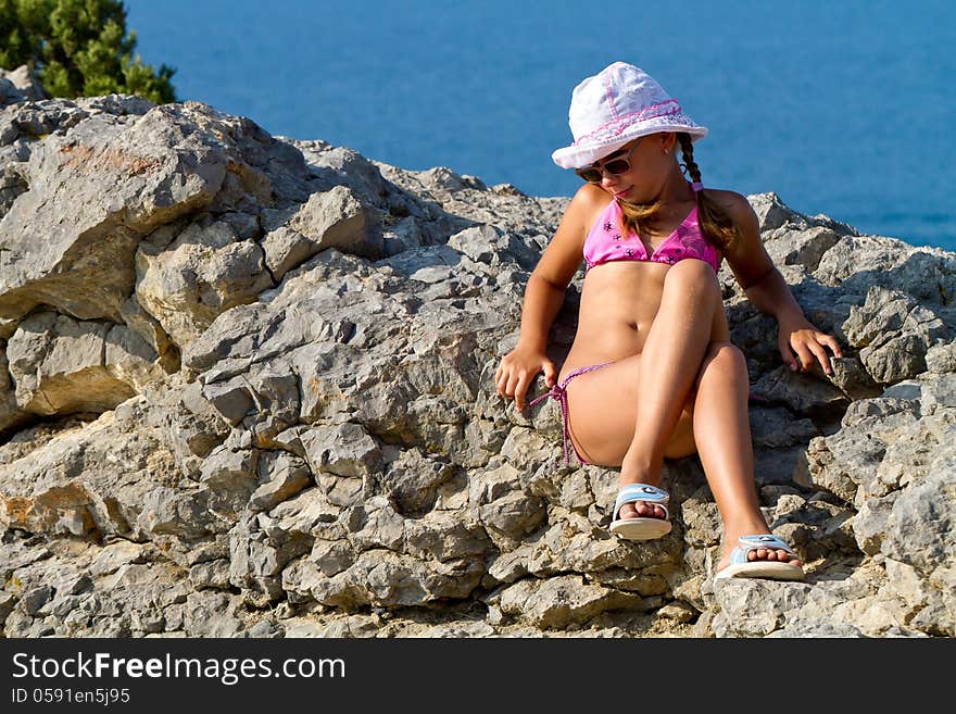 Girl 8 years with white hat and glasses sitting on the rocks by the sea. Girl 8 years with white hat and glasses sitting on the rocks by the sea