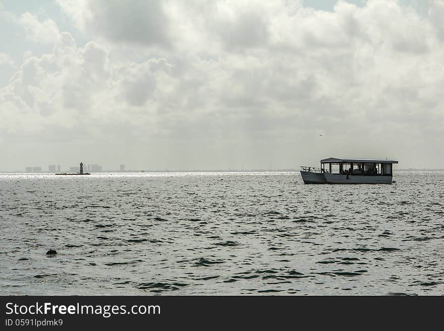 The sun is reflecting off the water and the light house while a boat floats on by off of Isla Mujeres, Mexico. With Cancun in the background. The sun is reflecting off the water and the light house while a boat floats on by off of Isla Mujeres, Mexico. With Cancun in the background.