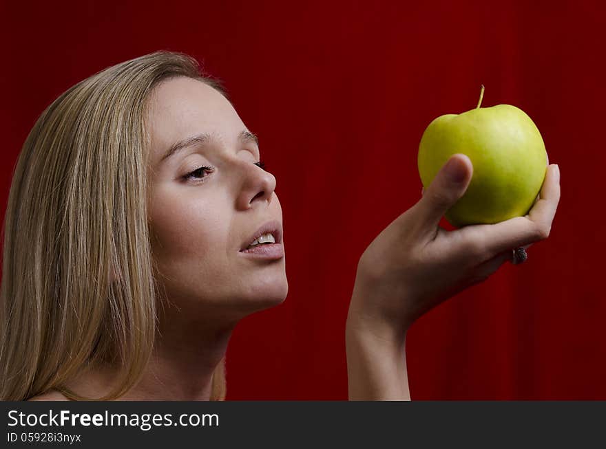 Young blonde woman holding a green apple on red background. Young blonde woman holding a green apple on red background