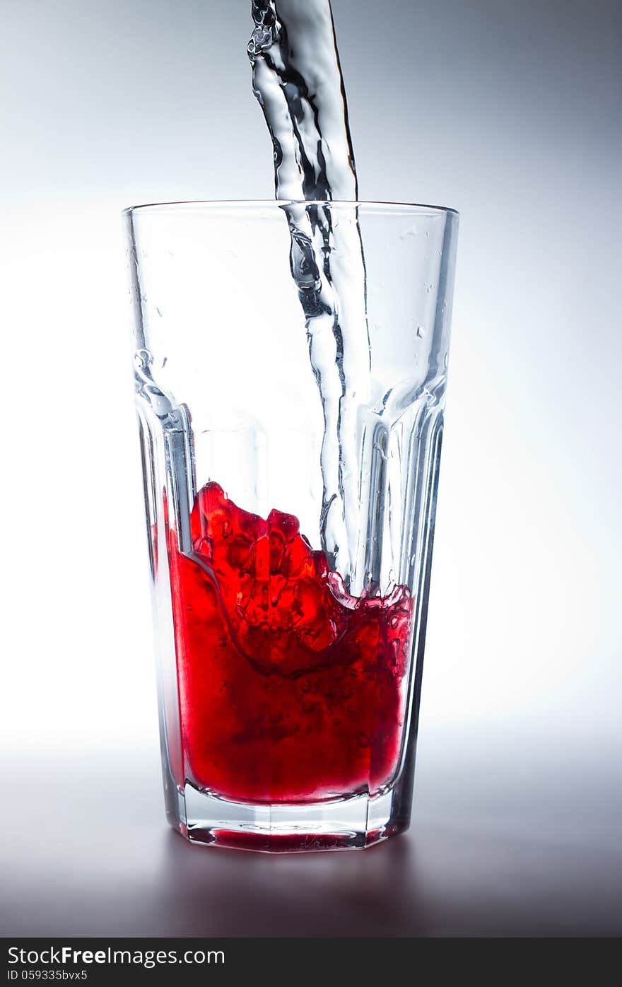 Water pouring into a glass with red juice. Water pouring into a glass with red juice