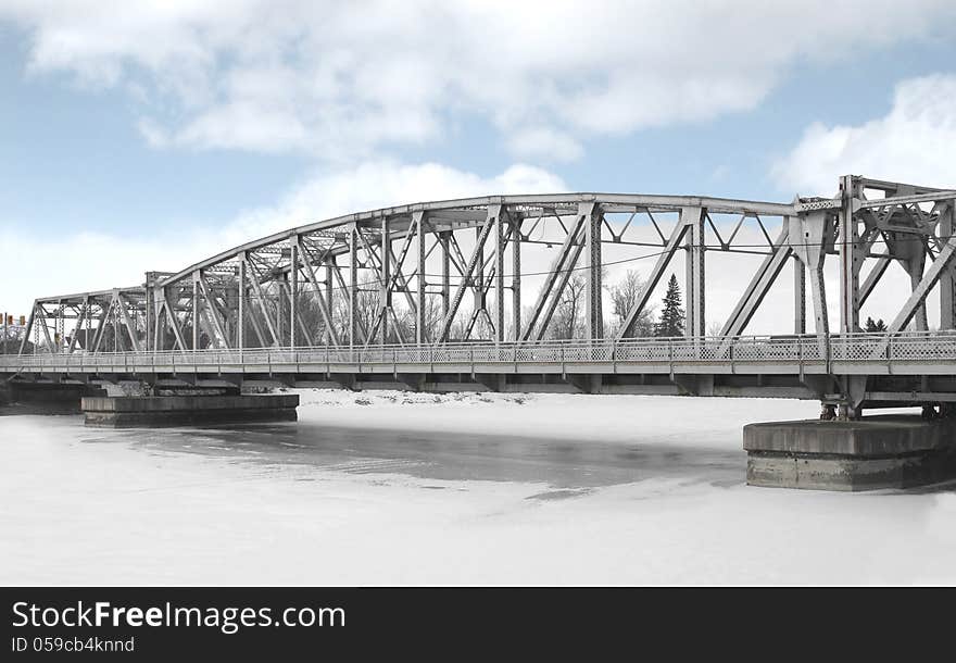 Long gray metal girder car bridge in winter over a frozen river. Long gray metal girder car bridge in winter over a frozen river.