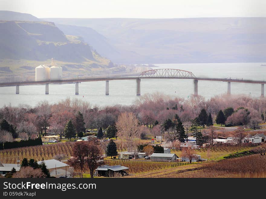 View of a groomed peaceful riverside neighborhood community in winter with buildings, barren trees, bridge over river, distant hills and a grain elevator. View of a groomed peaceful riverside neighborhood community in winter with buildings, barren trees, bridge over river, distant hills and a grain elevator.