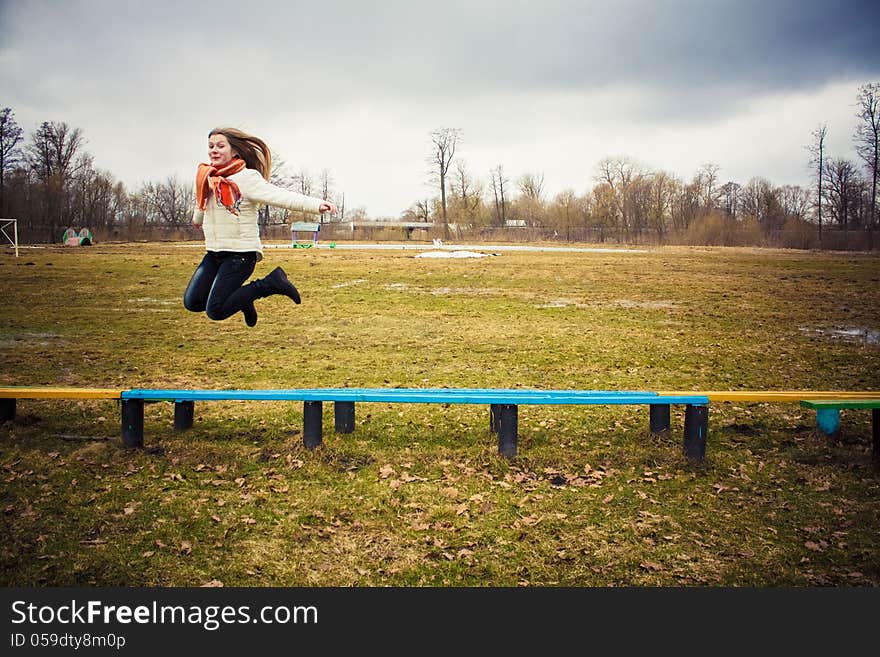 Teen Girl Wearing Orange Scarf Jumping Over Bench In Windy Day. Teen Girl Wearing Orange Scarf Jumping Over Bench In Windy Day