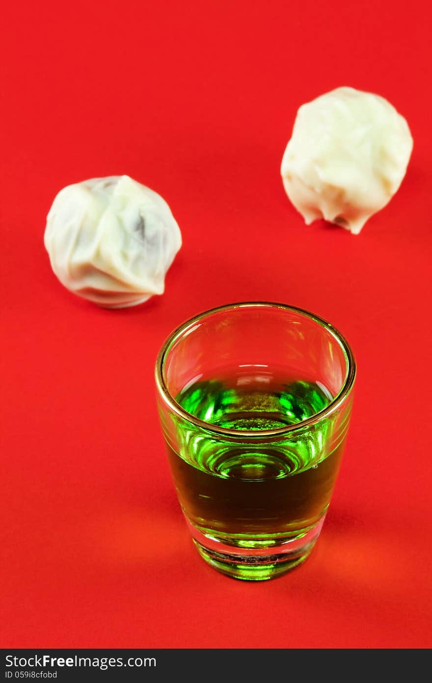 Glass with green liquor and white chocolate on a red background. Glass with green liquor and white chocolate on a red background