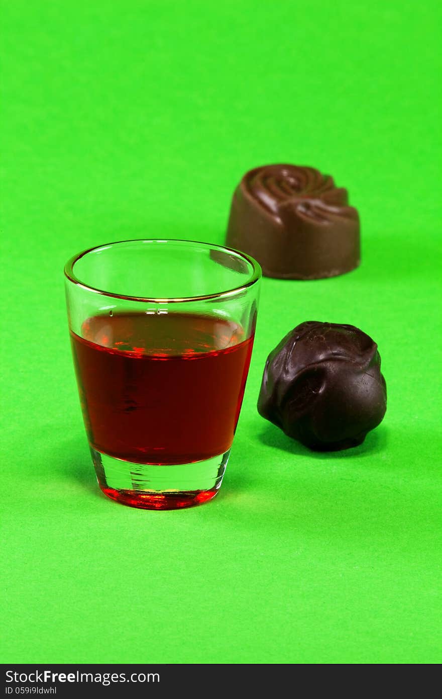 Glass with red liqueur and dark chocolate on a green background. Glass with red liqueur and dark chocolate on a green background