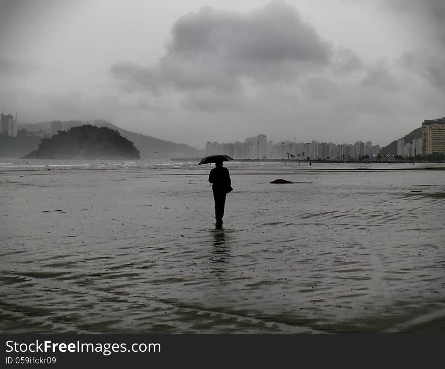 A man walking at the beach of Santos during a rainy day. A man walking at the beach of Santos during a rainy day