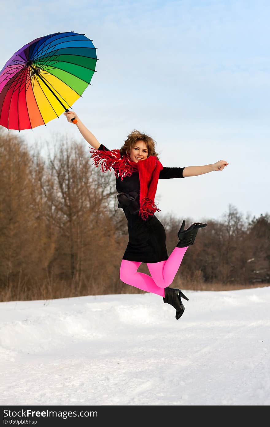 Young blond beautiful woman jumping against wood in bright scarf with color umbrella in winter. Young blond beautiful woman jumping against wood in bright scarf with color umbrella in winter