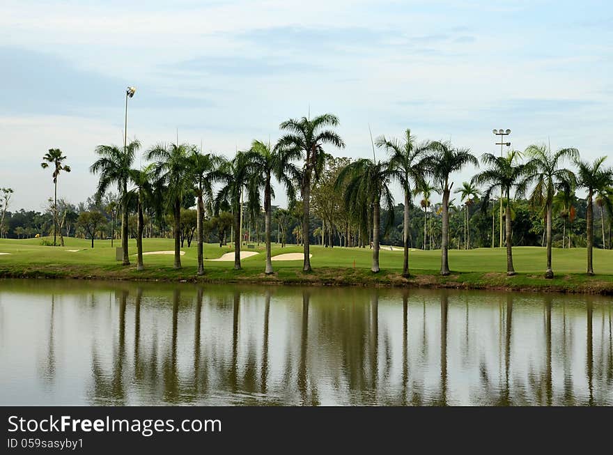 A scenic view of a golf course looking over a lake, showing sand traps, palm trees, clear blue sky and some golfers. A scenic view of a golf course looking over a lake, showing sand traps, palm trees, clear blue sky and some golfers.