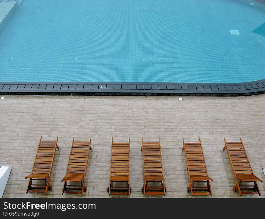 Wooden deckchairs around a swimming pool. Wooden deckchairs around a swimming pool