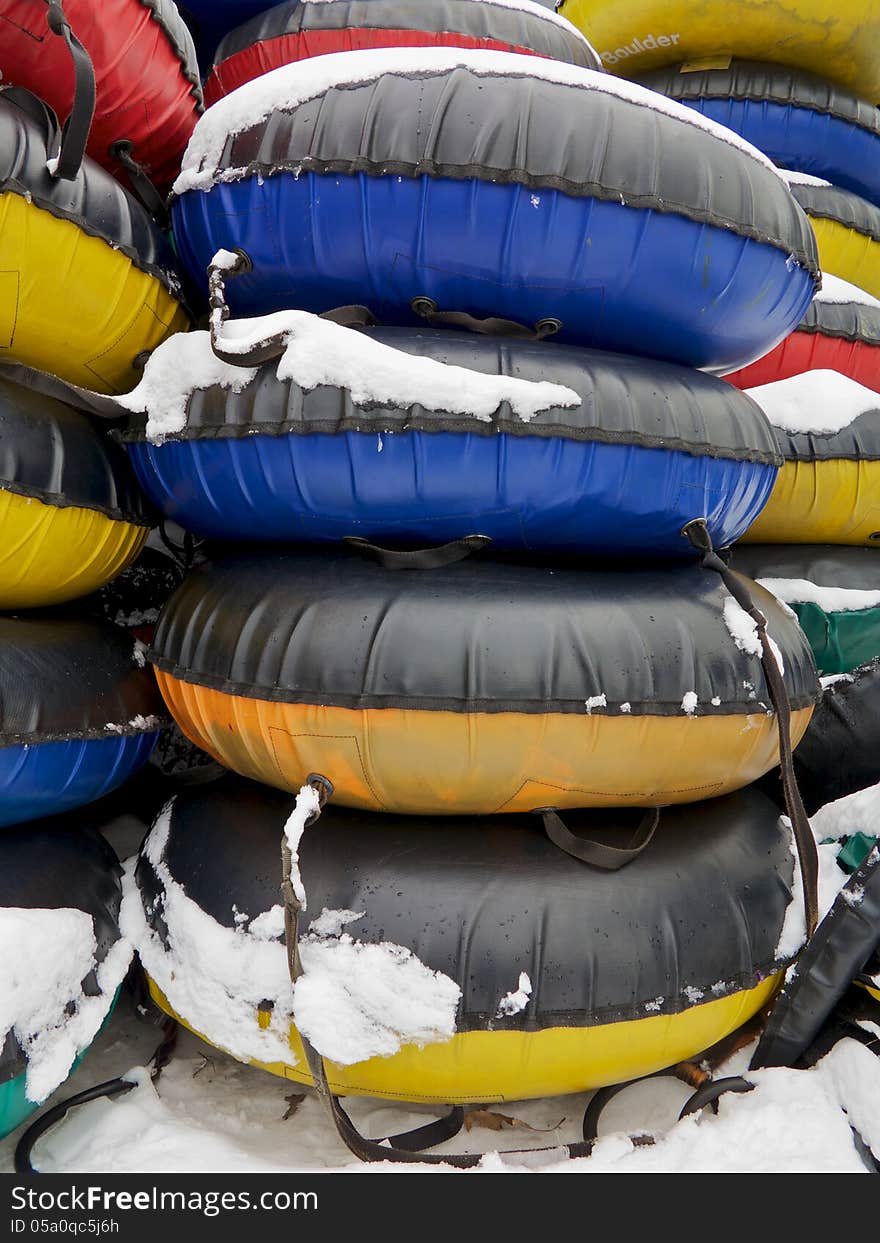 Stacks of red, yellow, blue, and green snow tubes are shown in the snow, vertical shot. Stacks of red, yellow, blue, and green snow tubes are shown in the snow, vertical shot.