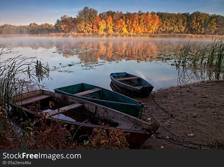 Boats on the quiet autumn lake, yellow forest, calm water