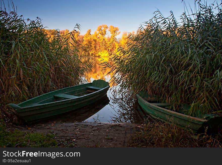 Boats on the quiet autumn lake, yellow forest, calm water