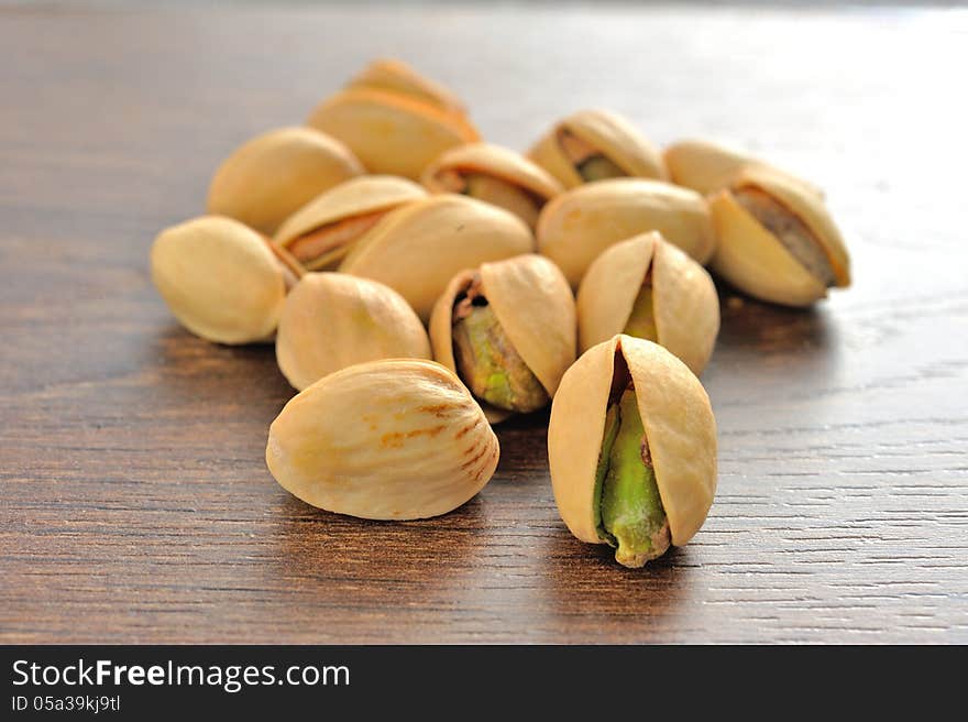 Roasted salted pistachios are a small pile on brown wooden table. Roasted salted pistachios are a small pile on brown wooden table