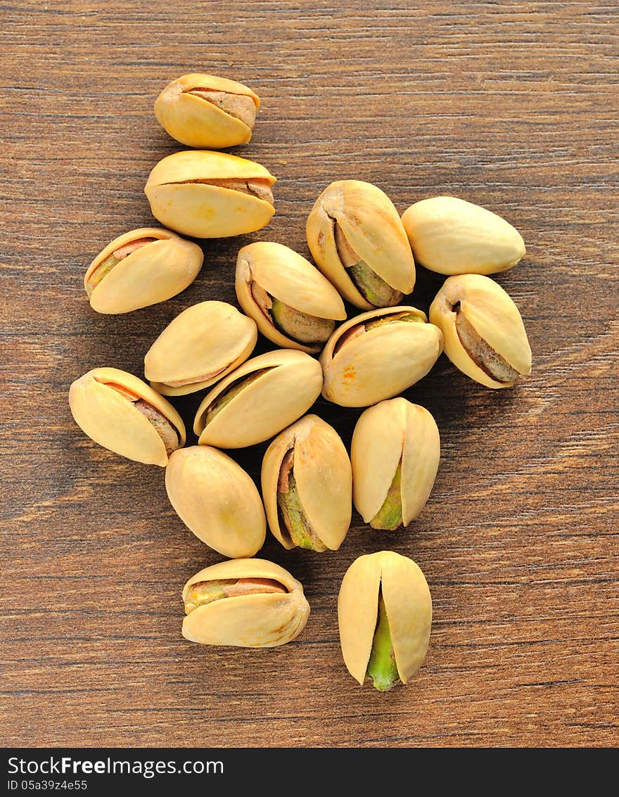 Roasted salted pistachios are a small pile on brown wooden table