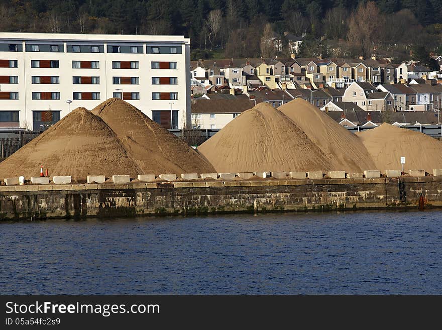 Mounds of sand awaiting collection standing on dockside with buildings and houses in background. Mounds of sand awaiting collection standing on dockside with buildings and houses in background.
