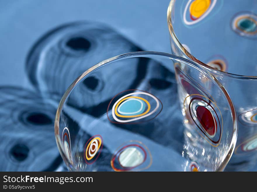 Two glasses in the bottom right of frame cast shadows upward onto a blue background. Two glasses in the bottom right of frame cast shadows upward onto a blue background.