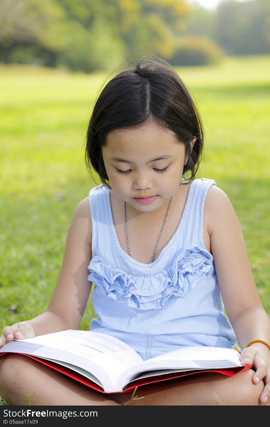 Asian little girl reading book in the park