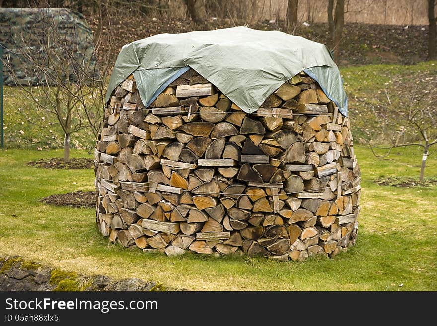 Chopped wood piled round mast, pile of wood covered with a tarpaulin. Chopped wood piled round mast, pile of wood covered with a tarpaulin