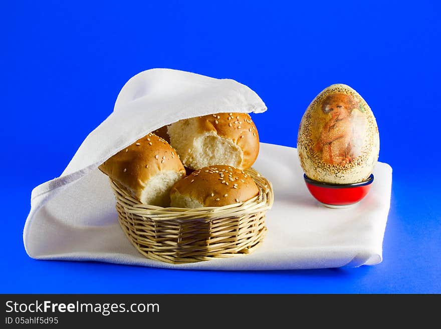 Easter treat - buns in a basket on a white napkin, and Easter egg, blue background. Easter treat - buns in a basket on a white napkin, and Easter egg, blue background