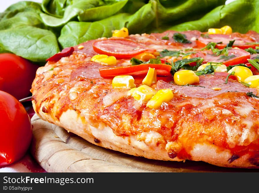 salami pizza sitting on wooden cutting board with tomatoes and salad