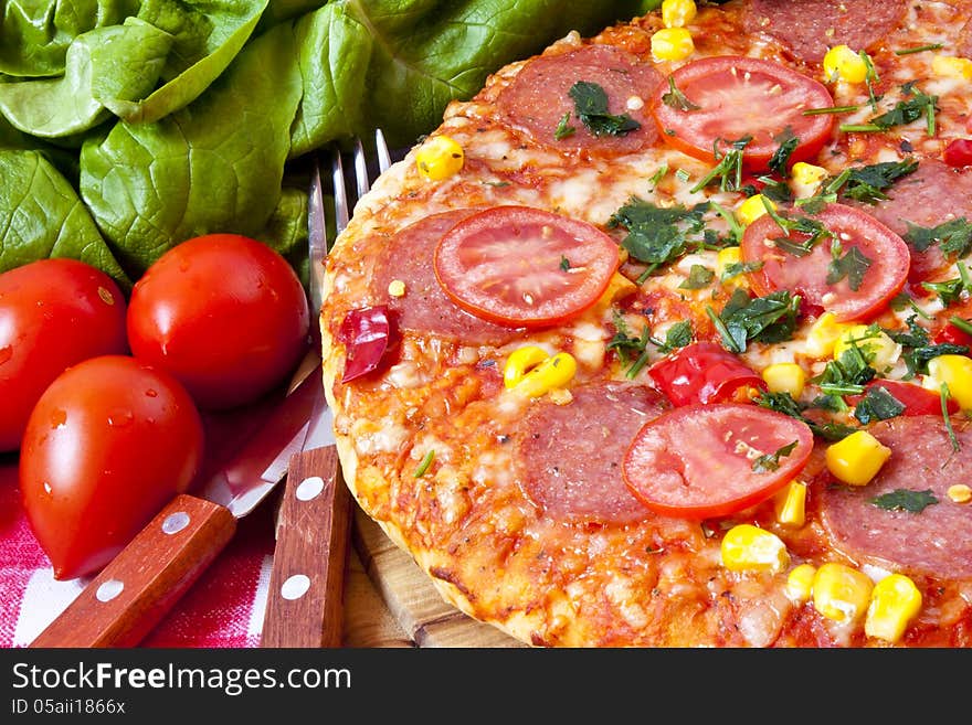 Salami pizza sitting on wooden cutting board with tomatoes and salad