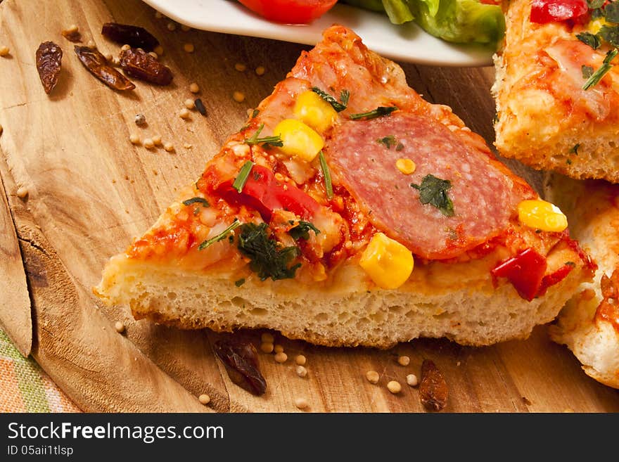 Slice of salami pizza sitting on wooden cutting board