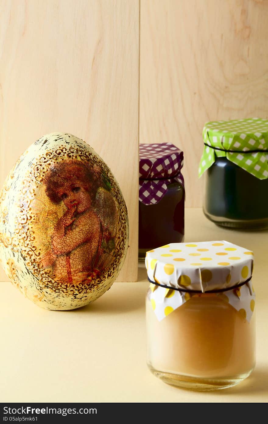 Three small jars with homemade jams and decorative Easter egg on light woody background. Three small jars with homemade jams and decorative Easter egg on light woody background