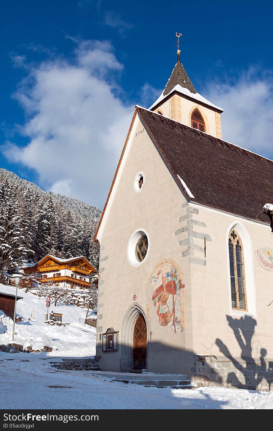 A wintertime view of a small church with a tall steeple in Vila di Sopra, Sud Tyrol