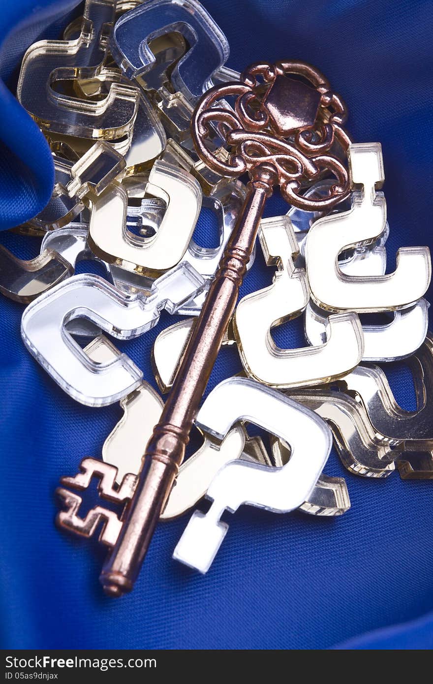 Key to all questions concept shot with gold and silver question marks, vintage skeleton key on a blue silk background.