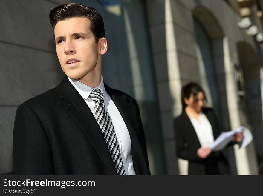 Portrait of attractive young businessman in the city with beautiful businesswoman in the background. Portrait of attractive young businessman in the city with beautiful businesswoman in the background