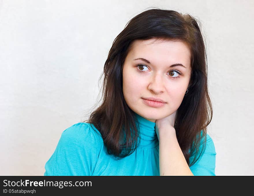 Close-up portrait of a young beautiful brunette girl thoughtfully looks aside in the blue sweater