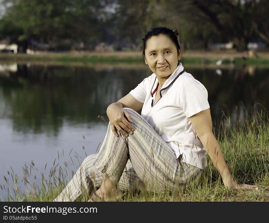 Woman sitting on green field by lake