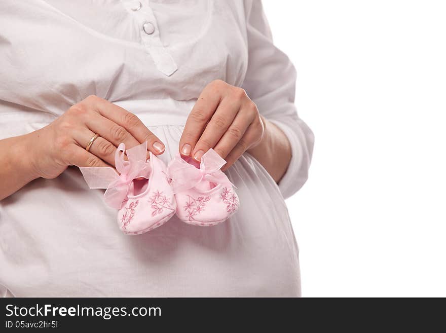 Pregnant woman keeping pink baby-shoes. Close up shot of belly and shoes.