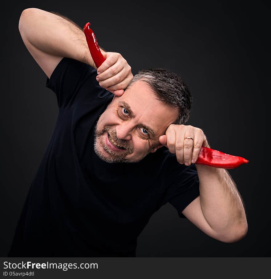 An elderly man holding two red hot chili peppers near the head like horns