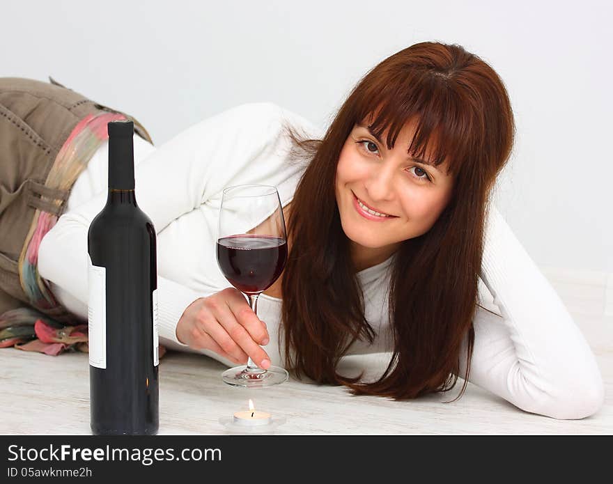 Beautiful, smiling woman relaxing with glass of red wine on the floor