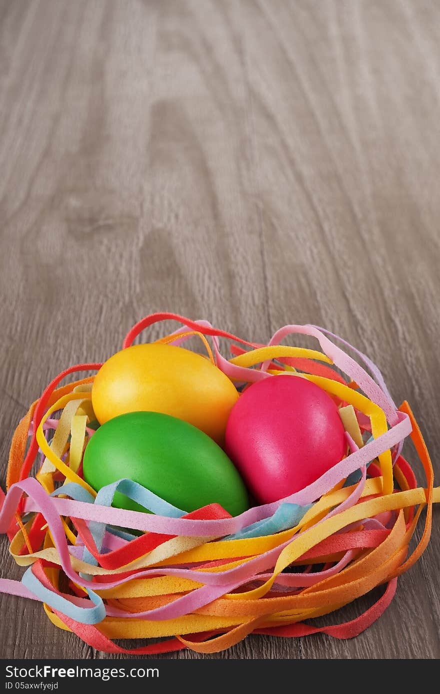 Multicolored easter eggs in the nest on old wooden table