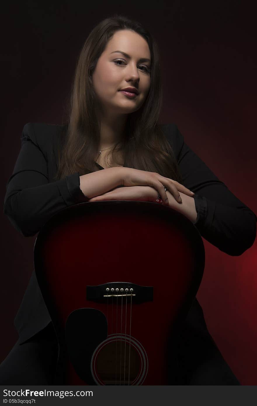 Portrait of young woman with her hands on guitar body, isolated on dark background. Portrait of young woman with her hands on guitar body, isolated on dark background