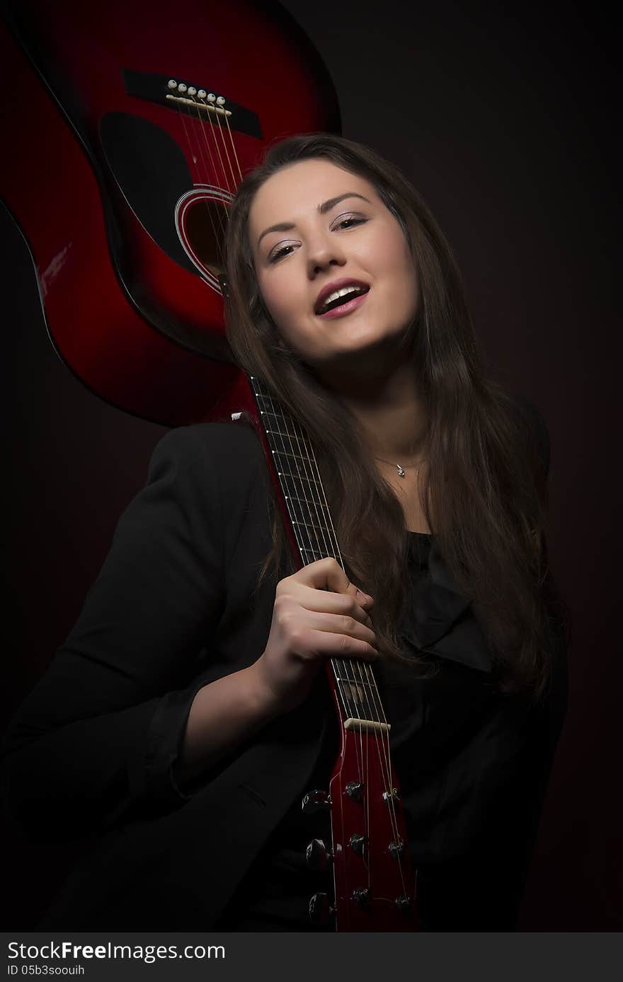 Portrait of young self-confident expressive woman holding red color guitar upside down, isolated on dark background. Portrait of young self-confident expressive woman holding red color guitar upside down, isolated on dark background