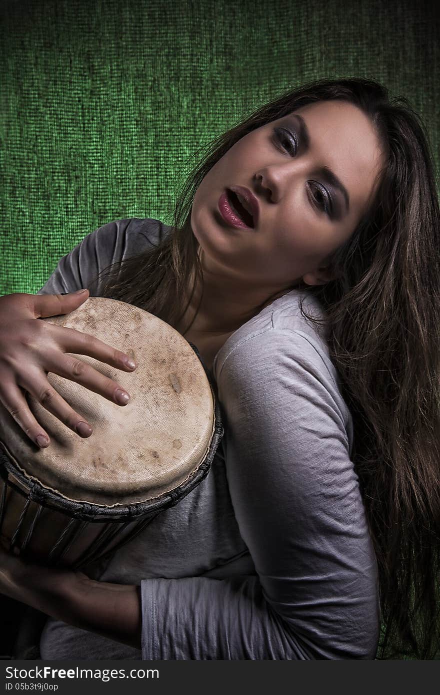 Portrait of beautiful expressive long hair brunette woman playing djembe drum, on isolated lightened up green background. Portrait of beautiful expressive long hair brunette woman playing djembe drum, on isolated lightened up green background