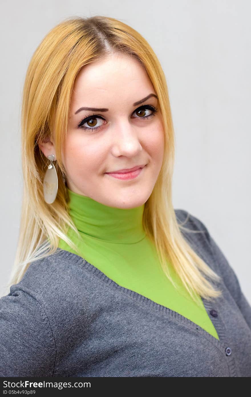 Close-up portrait of a lovely blonde smiling girl with long hair in green turtleneck and gray cardigan