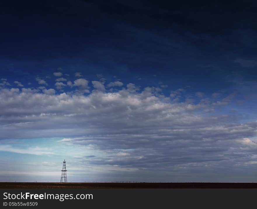 Abandoned oil rig profiled on cloudy day sky in an active oilfield