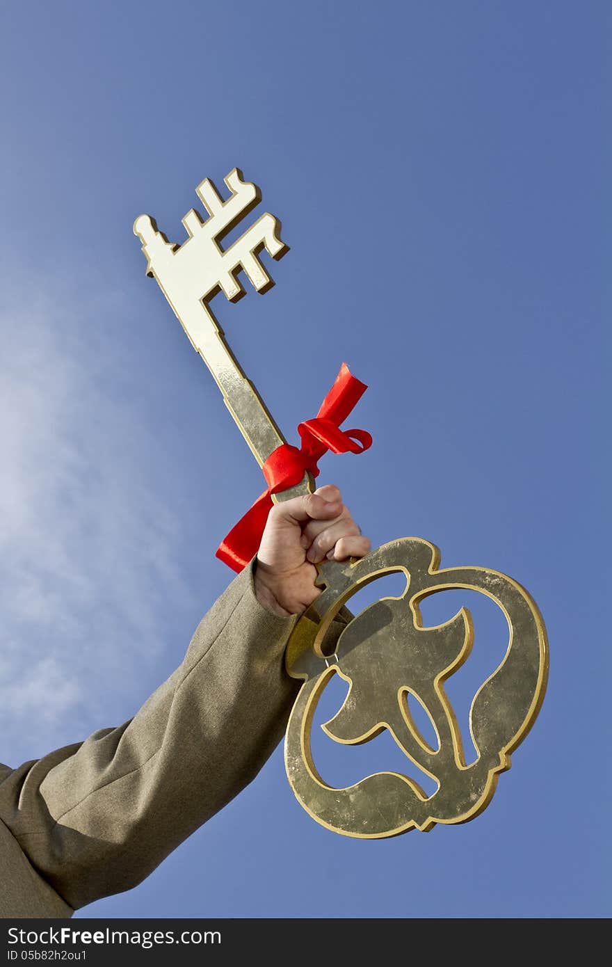 Hand holding golden key with a red bow on it & blue sky background. Hand holding golden key with a red bow on it & blue sky background.