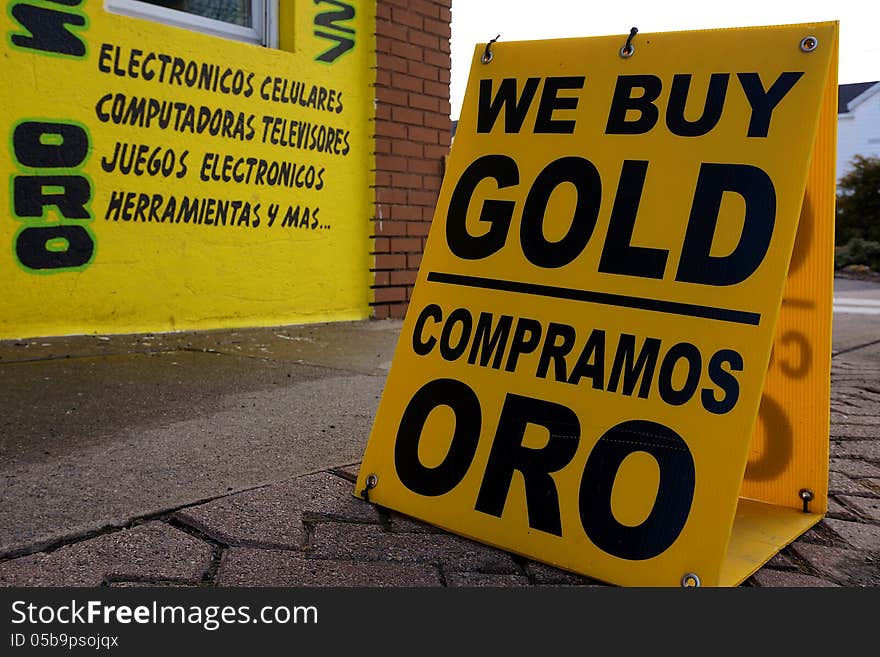 English and Spanish We Buy Gold sign on street with bright yellow wall in background. English and Spanish We Buy Gold sign on street with bright yellow wall in background.