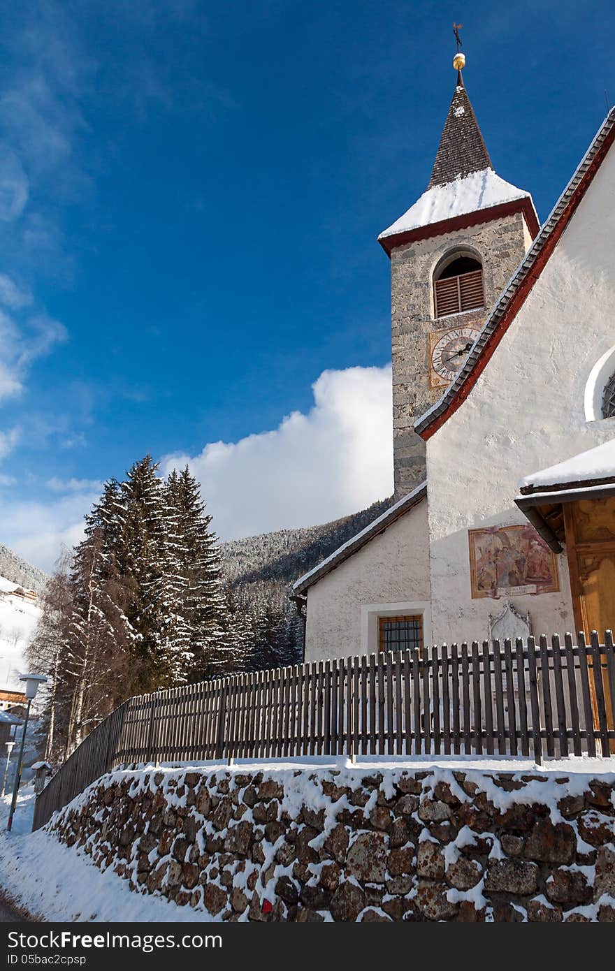 A wintertime view of a small church with a tall steeple in Montassilone, Sud Tyrol