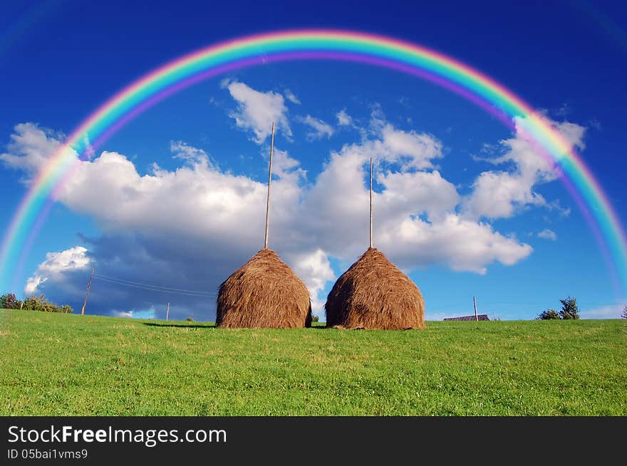 Summer mountain village landscape with a rainbow over haystacks. Summer mountain village landscape with a rainbow over haystacks